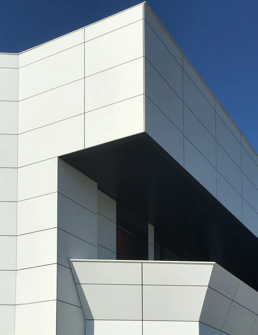 Esquina de la fachada de La Estación, en Las Rozas, con paneles blancos y alero oscuro contra el cielo