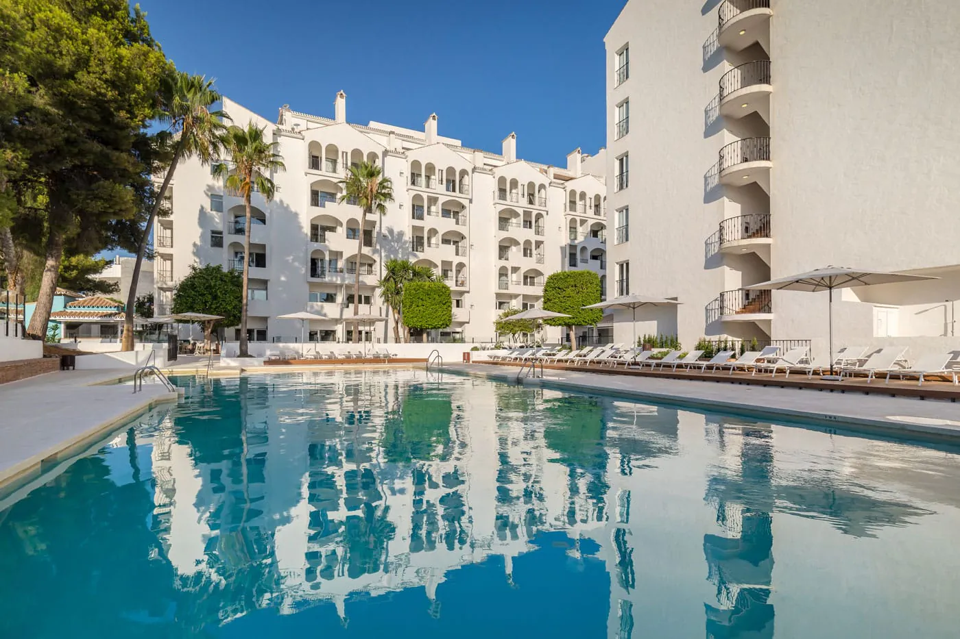 Piscina del Hotel Occidental Puerto Banús reflejando la fachada blanca del hotel rehabilitado entre palmeras