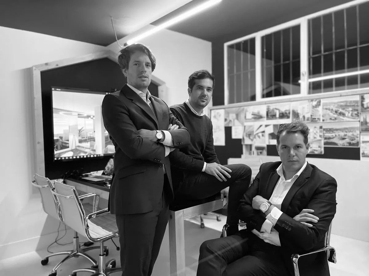Los tres socios fundadores de dhoce, con traje, en el estudio frente a pantallas con proyectos